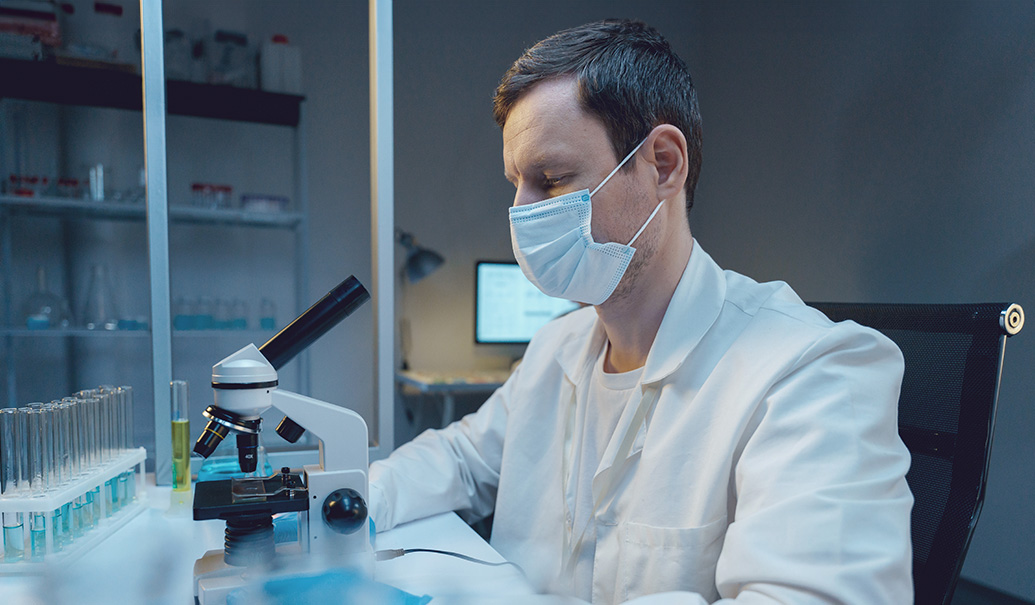 A biologist in a lab coat working with a microscope