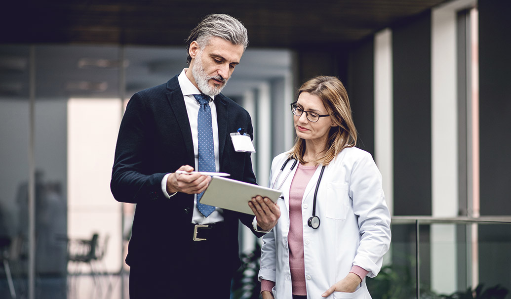 Pharmaceutical-sales-representative-with-tablet-talking-to-doctor