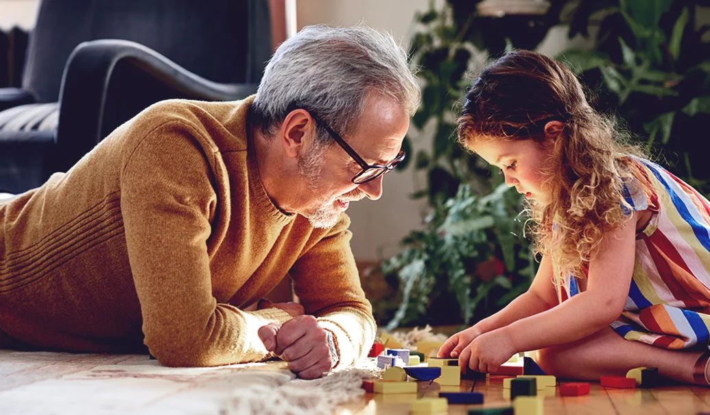 Senior man watches granddaughter with toy blocks